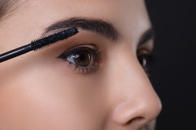 Photo of Beautiful young woman applying mascara on black background, closeup