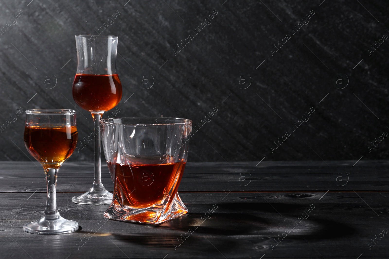 Photo of Different delicious liqueurs in glasses on black wooden table, space for text