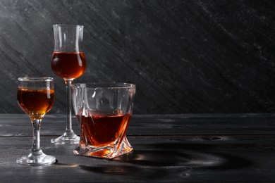 Different delicious liqueurs in glasses on black wooden table, space for text