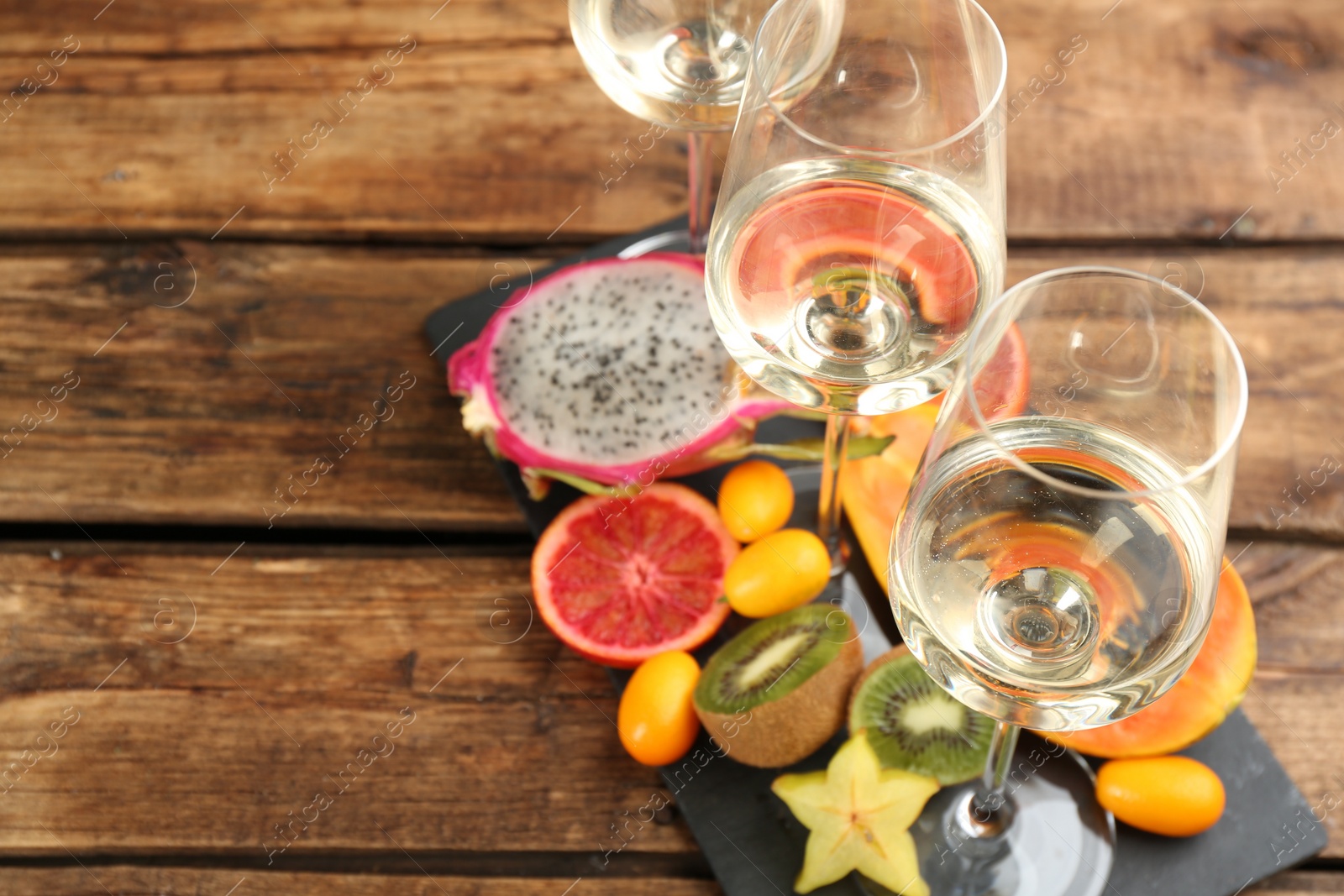 Photo of Delicious exotic fruits and wine on wooden table. Space for text