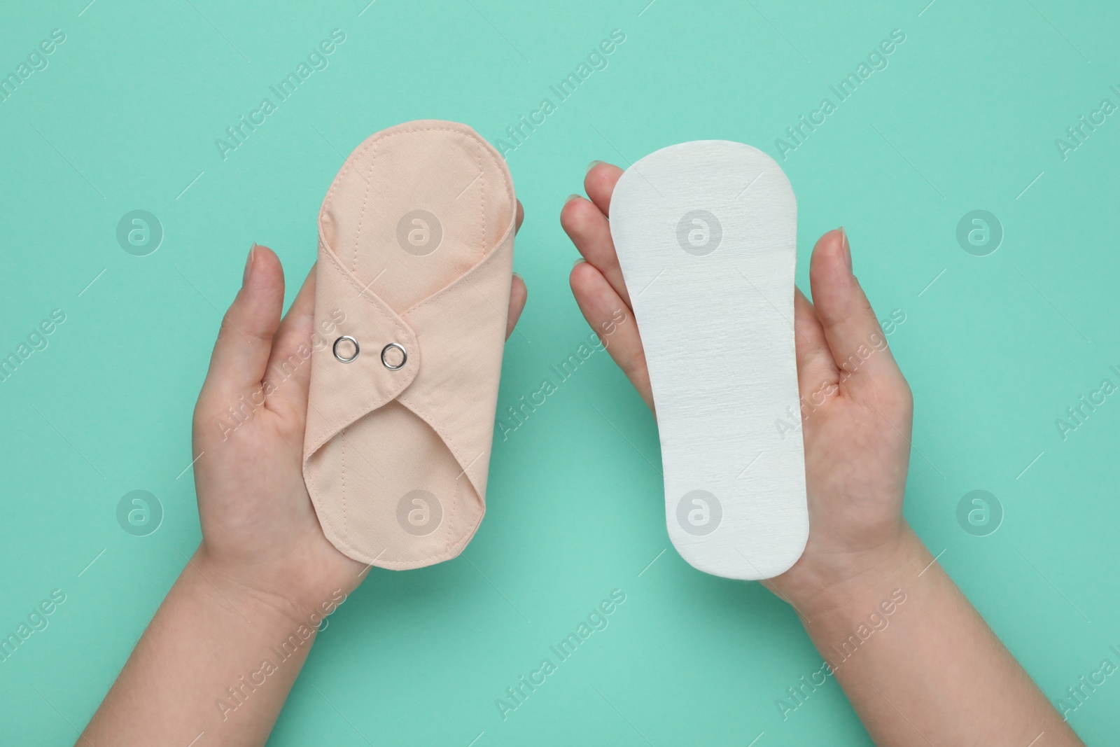 Photo of Woman holding disposable and reusable cloth menstrual pads on turquoise background, top view