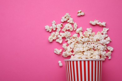 Photo of Overturned paper cup with delicious popcorn on pink background, flat lay. Space for text