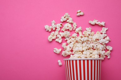 Overturned paper cup with delicious popcorn on pink background, flat lay. Space for text