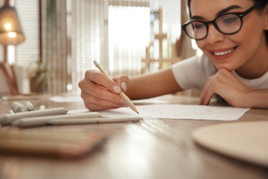 Photo of Young woman drawing with pencil at table indoors, focus on hand