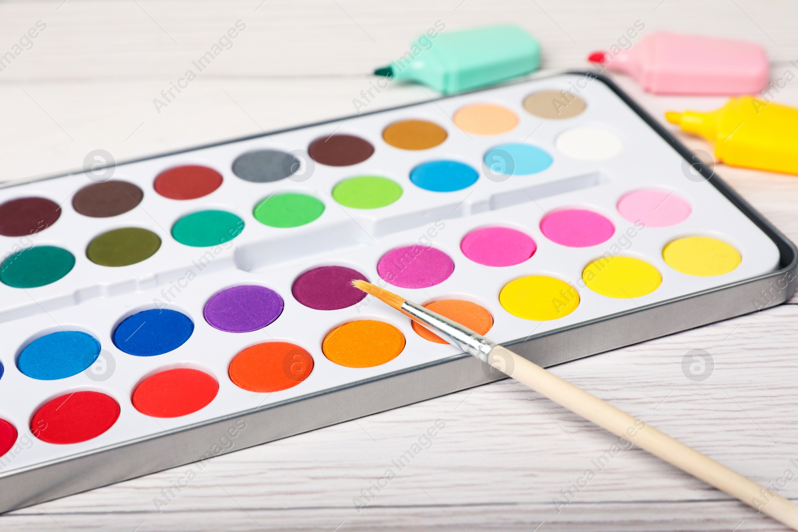 Photo of Watercolor palette with brush and colorful markers on white wooden table, closeup