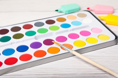 Photo of Watercolor palette with brush and colorful markers on white wooden table, closeup