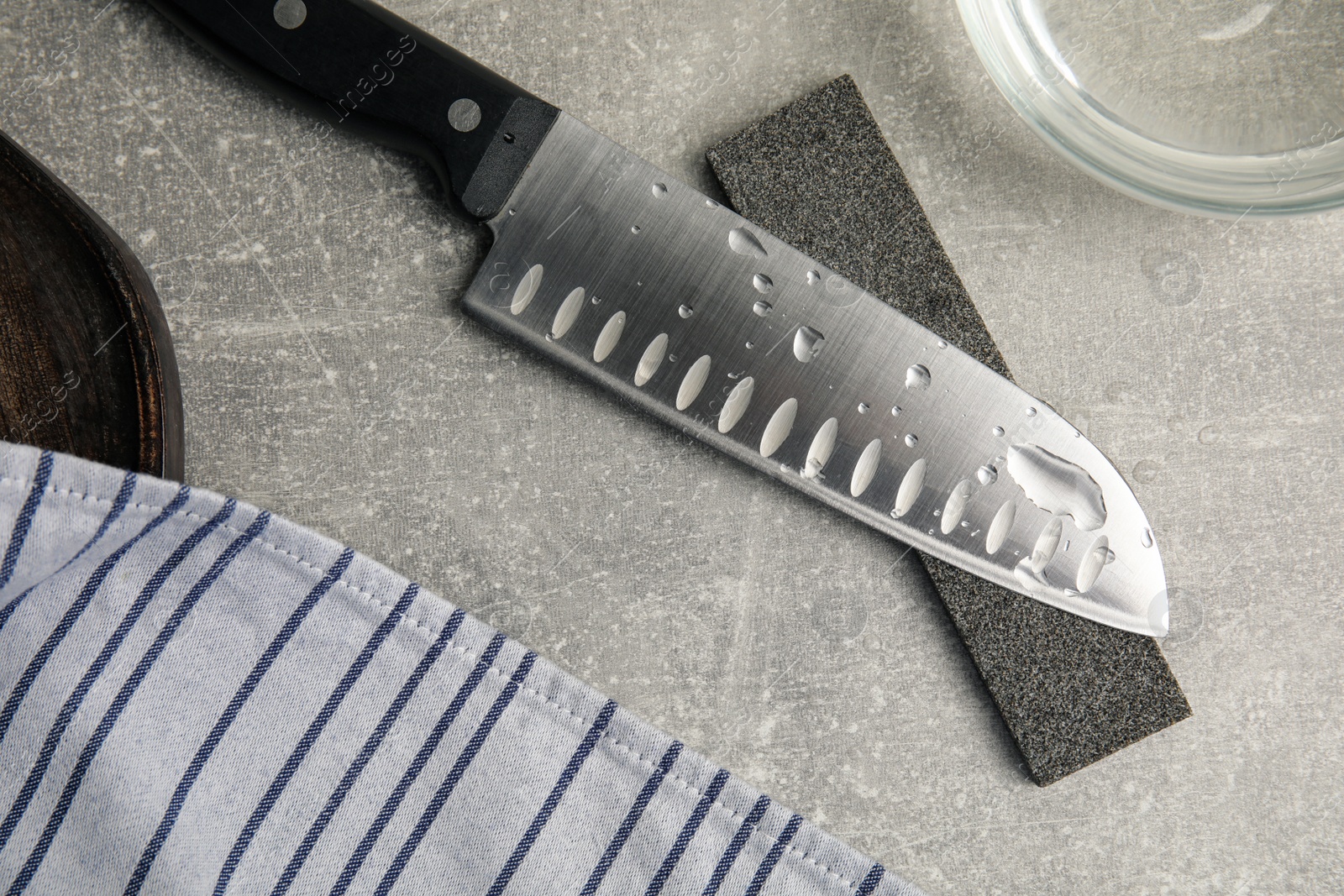 Photo of Sharpening stone, knife and water on grey table, flat lay
