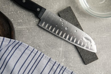 Photo of Sharpening stone, knife and water on grey table, flat lay