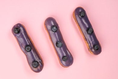 Photo of Delicious eclairs covered with glaze on pink background, top view