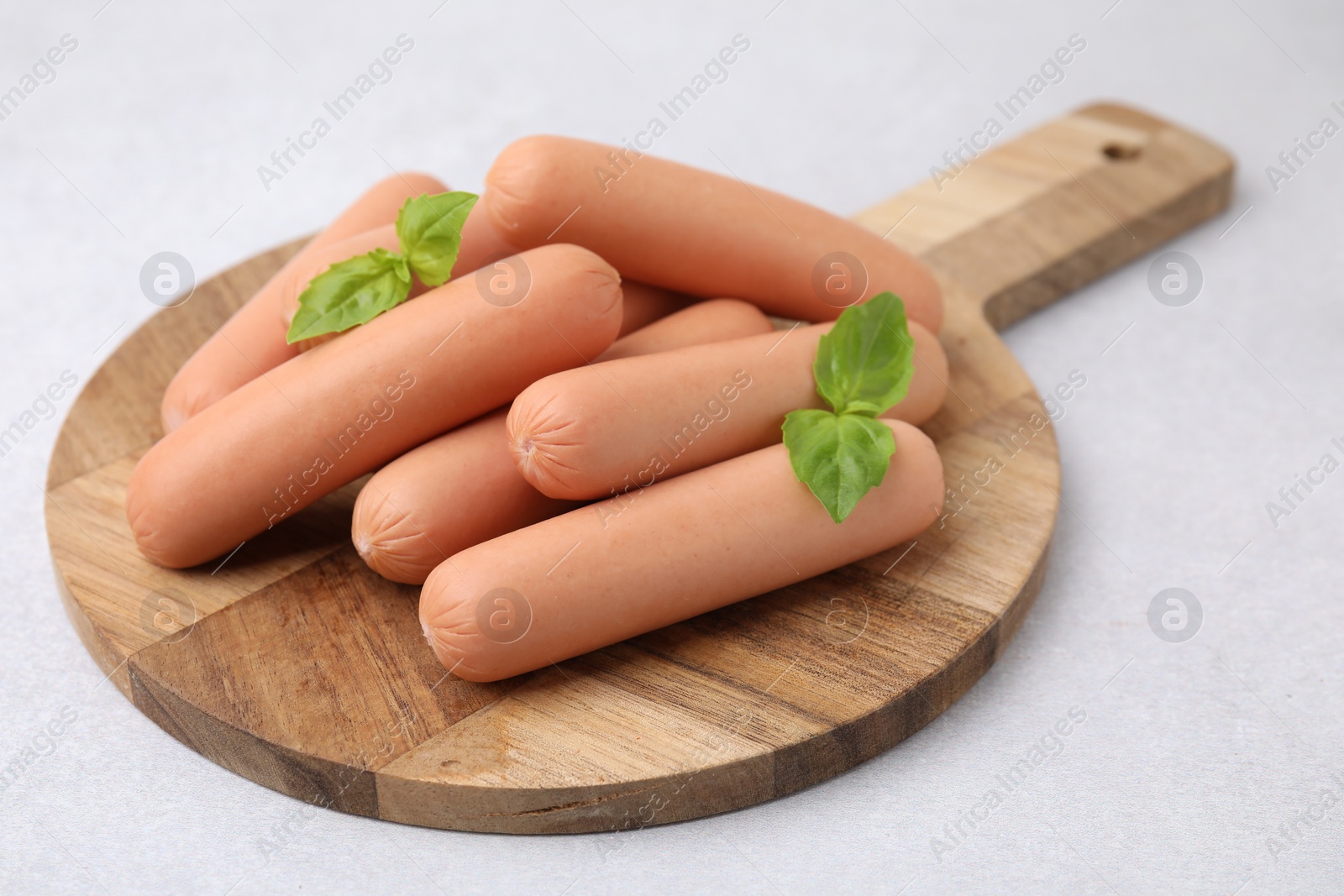 Photo of Delicious boiled sausages and basil on light gray table, closeup