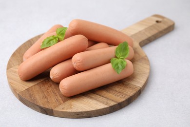 Delicious boiled sausages and basil on light gray table, closeup