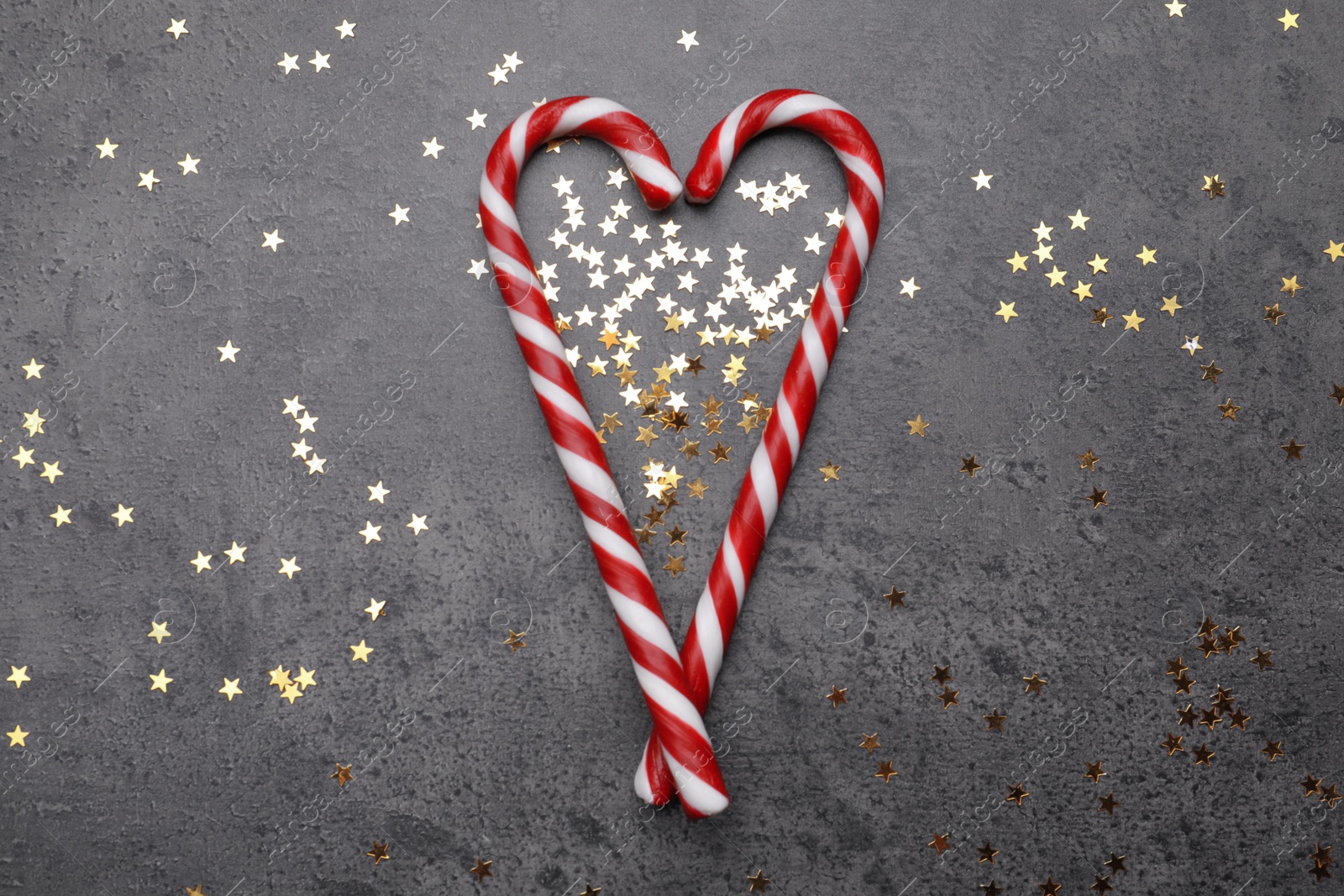 Photo of Heart made of sweet Christmas candy canes and shiny confetti on grey background, flat lay