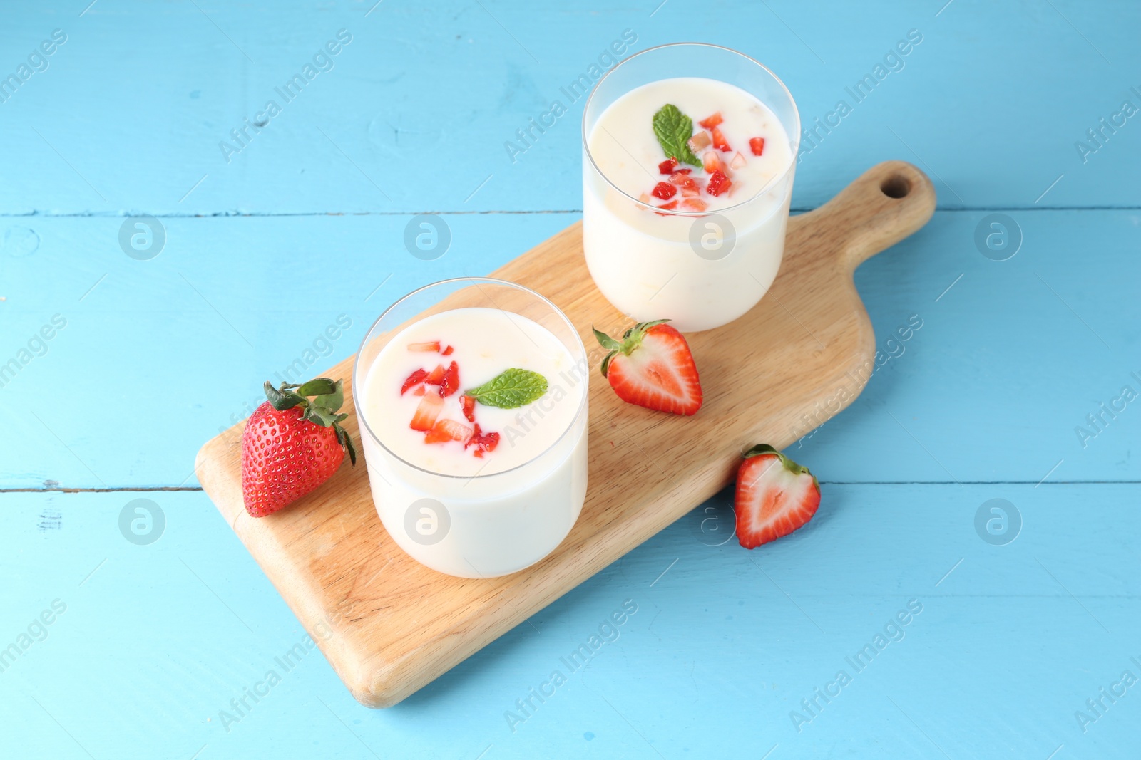 Photo of Tasty yogurt in glasses and strawberries on light blue wooden table