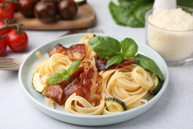 Tasty pasta with bacon and basil on light grey table