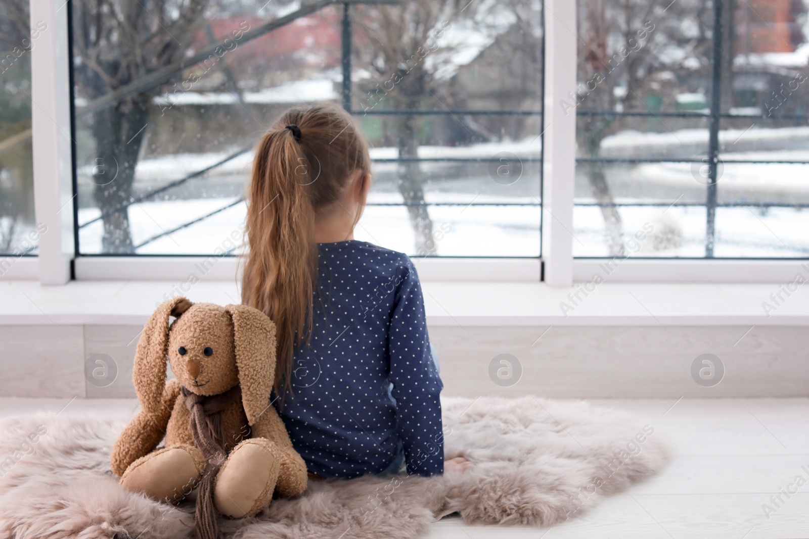 Photo of Lonely little girl with toy sitting near window indoors. Autism concept