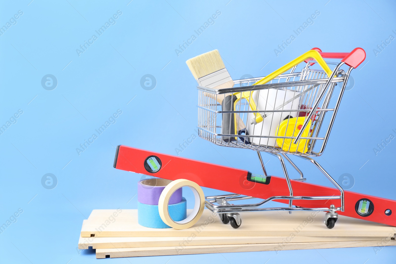 Photo of Small shopping cart with paint and renovation equipment on light blue background