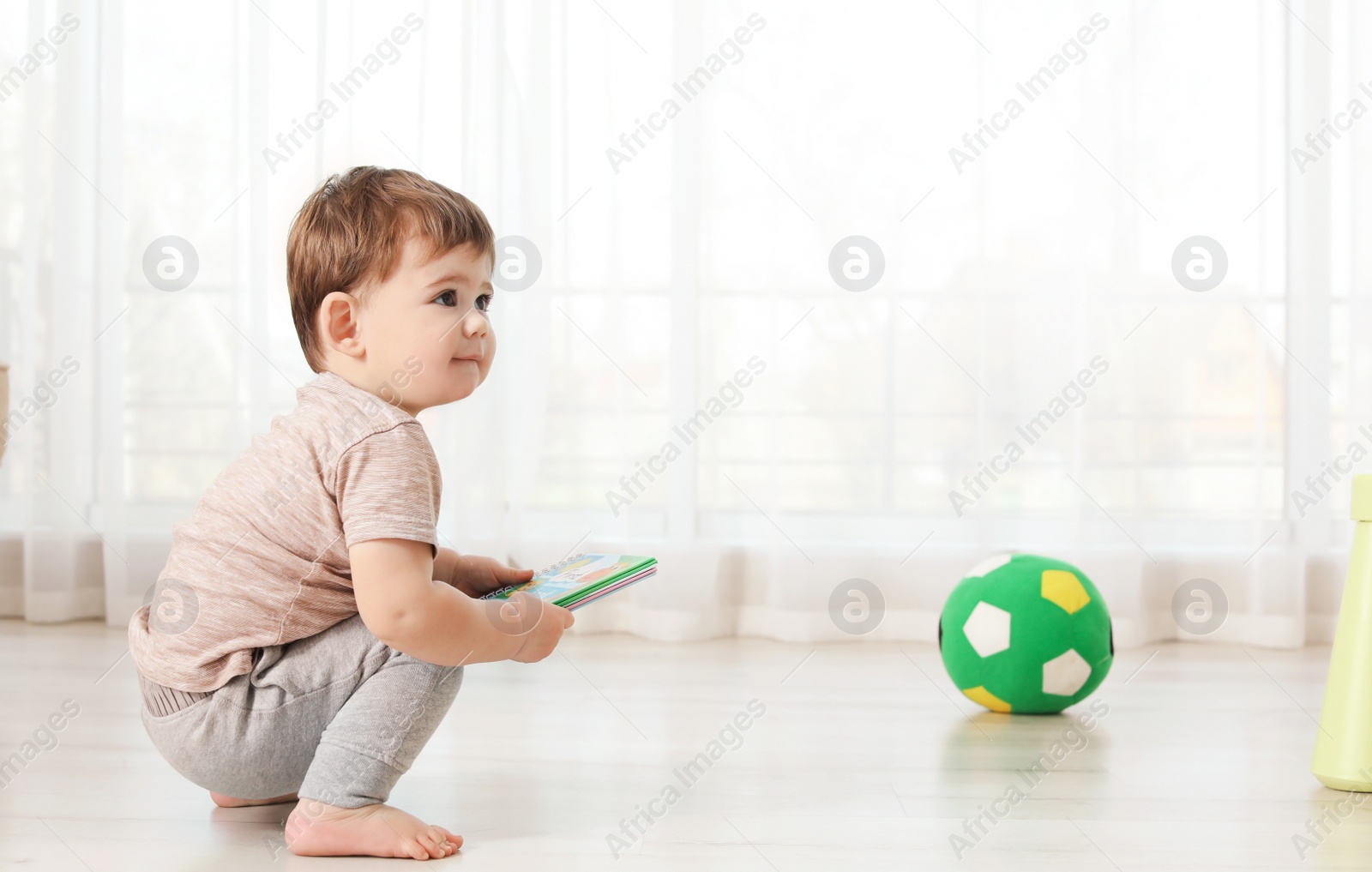 Photo of Cute baby sitting on floor with book at home