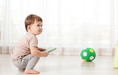 Cute baby sitting on floor with book at home