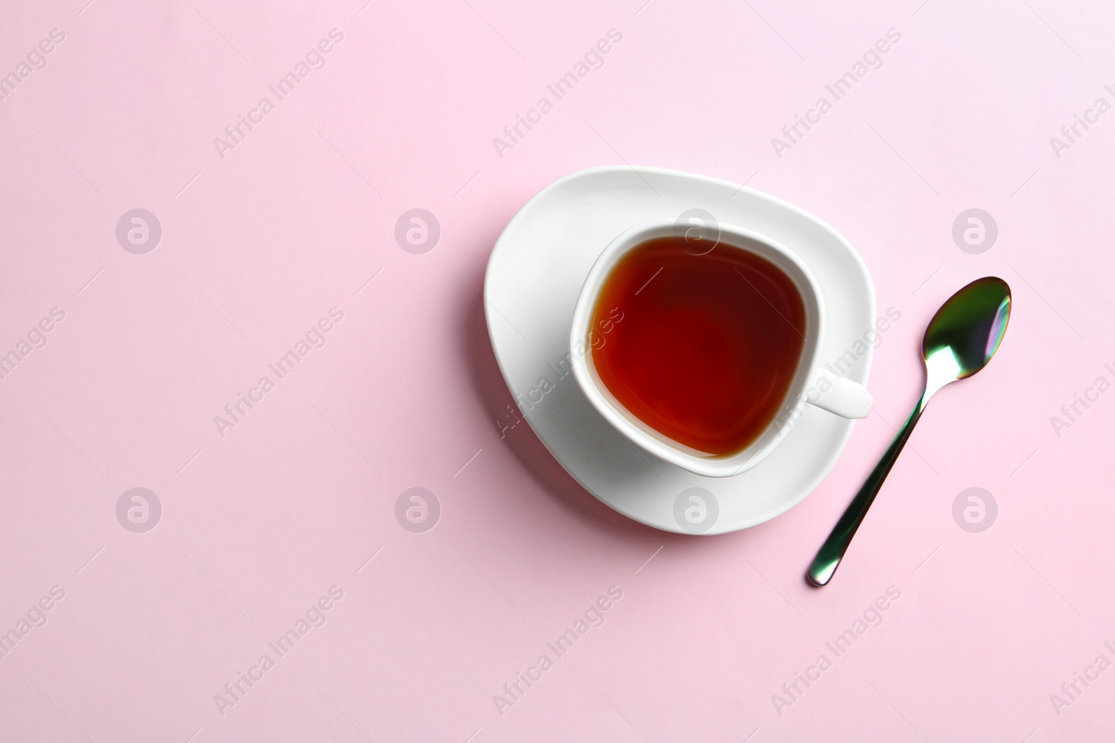 Photo of Cup of tea with saucer and spoon on pink background, flat lay. Space for text