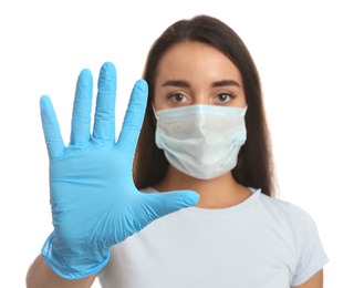 Photo of Woman in protective face mask and medical gloves showing stop gesture against white background, focus on hand