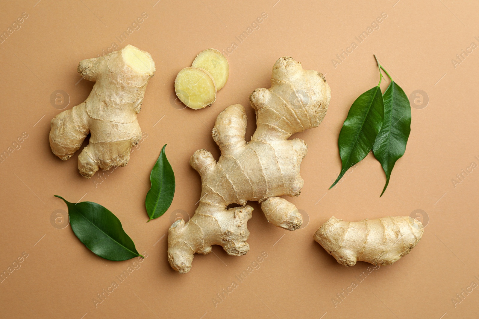 Photo of Fresh ginger with green leaves on light pale brown background, flat lay