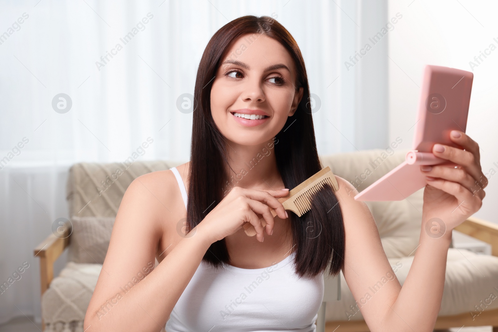 Photo of Beautiful woman brushing her hair and looking into compact mirror in room