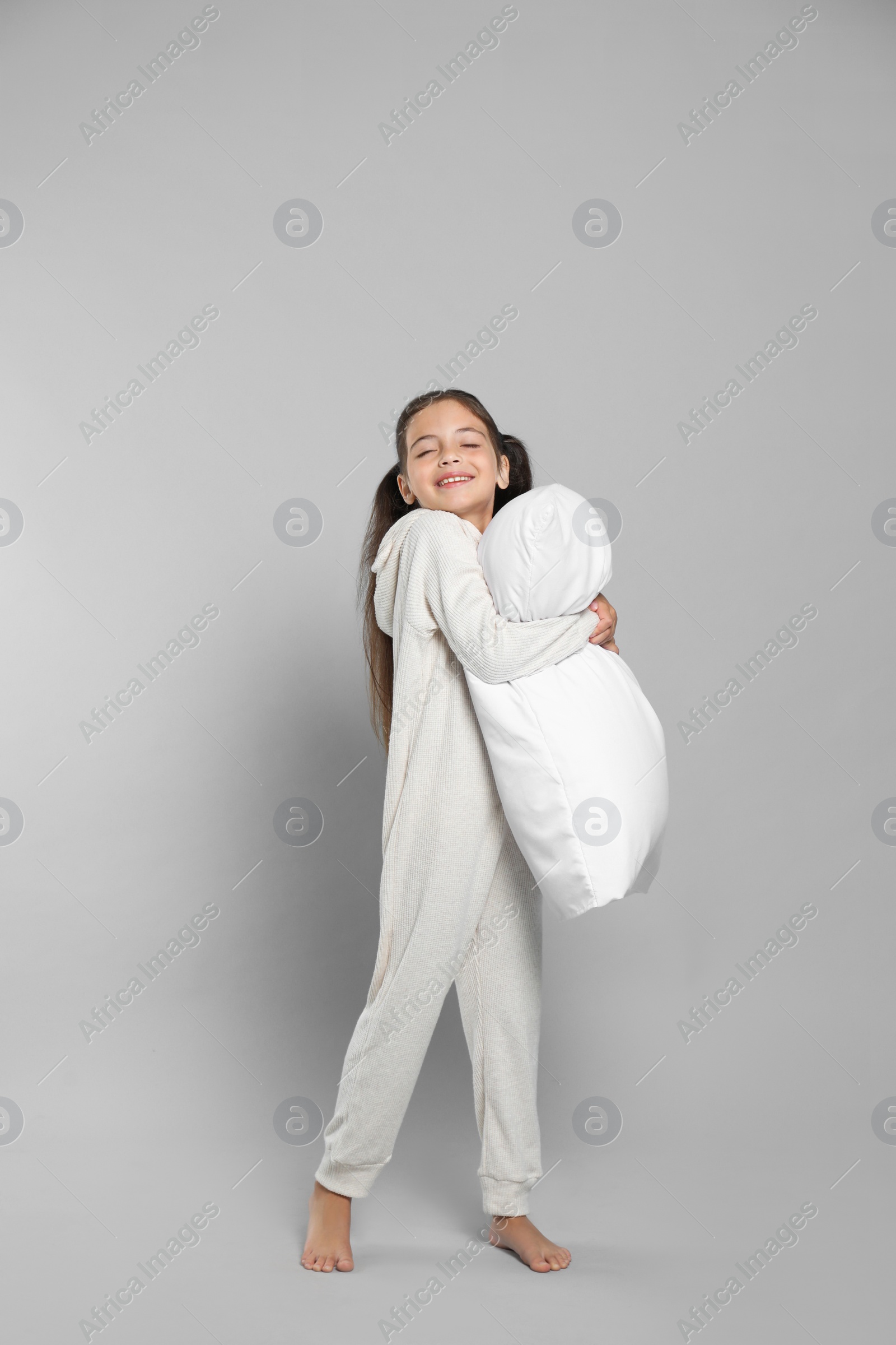 Photo of Cute girl in white pajamas hugging pillow on light grey background