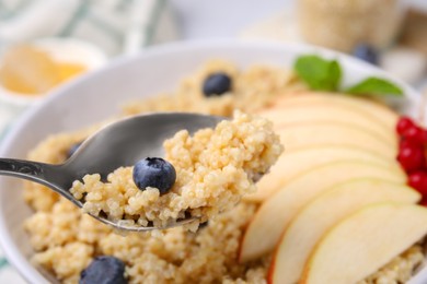 Photo of Spoon of delicious cooked quinoa with blueberry above bowl, closeup. Space for text