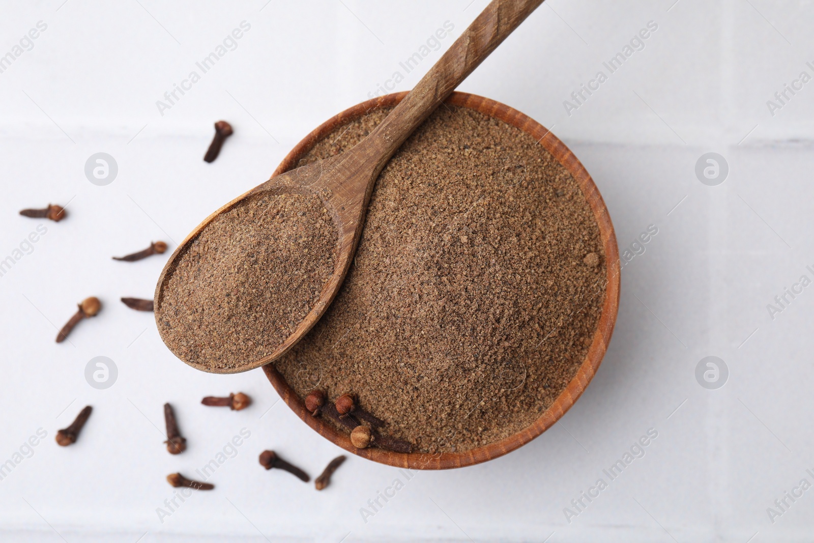 Photo of Aromatic clove powder and dried buds on white tiled table, top view