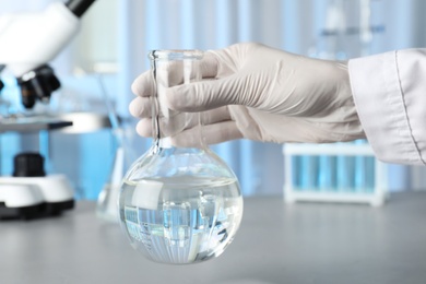 Scientist holding Florence flask with water, closeup. Laboratory analysis