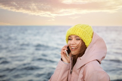 Photo of Young woman talking on mobile phone near sea