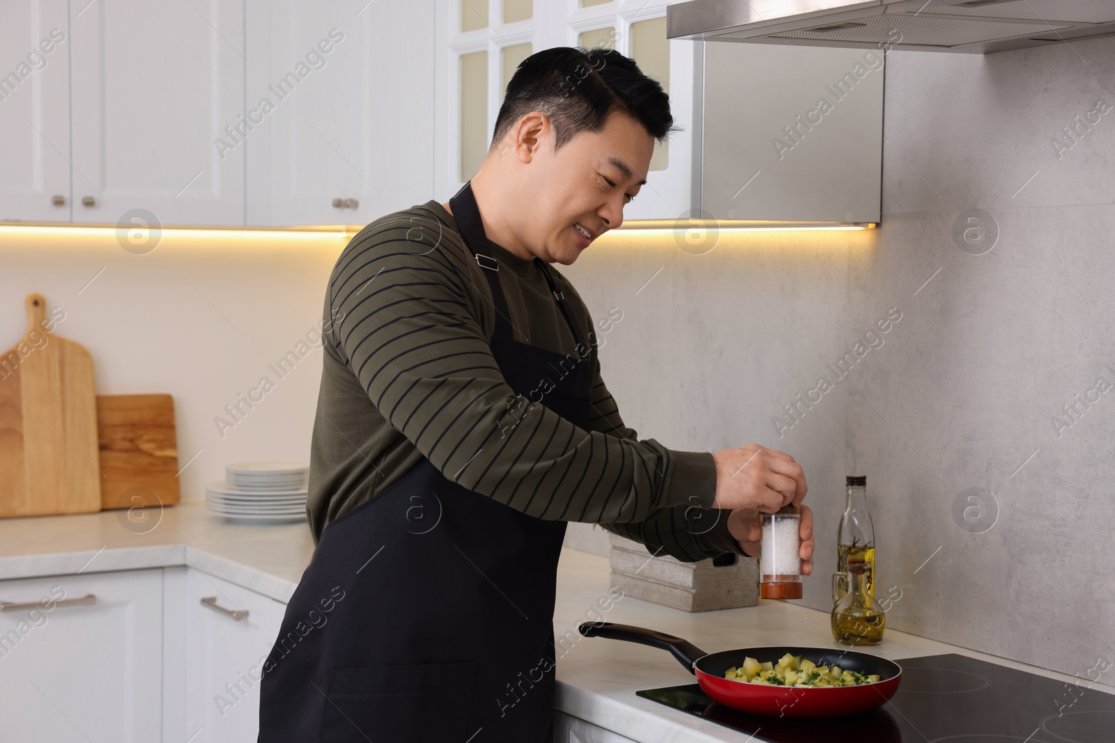Photo of Cooking process. Man adding salt into frying pan in kitchen