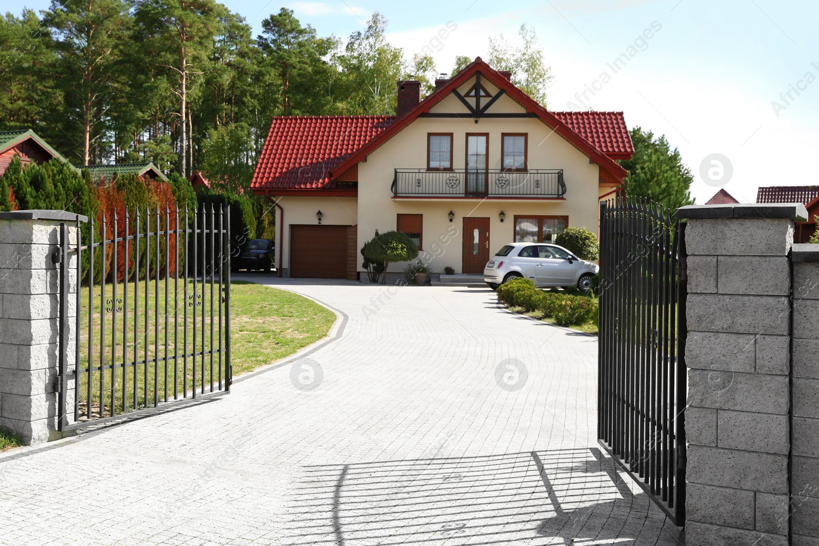 Photo of Open metal gates near houses and bushes on sunny day