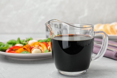 Photo of Balsamic vinegar in glass jug near plate with salad on table