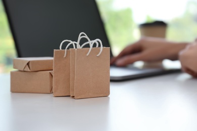 Internet shopping. Small bags and boxes near woman using laptop indoors, space for text