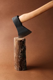 Metal ax in wooden log on brown background