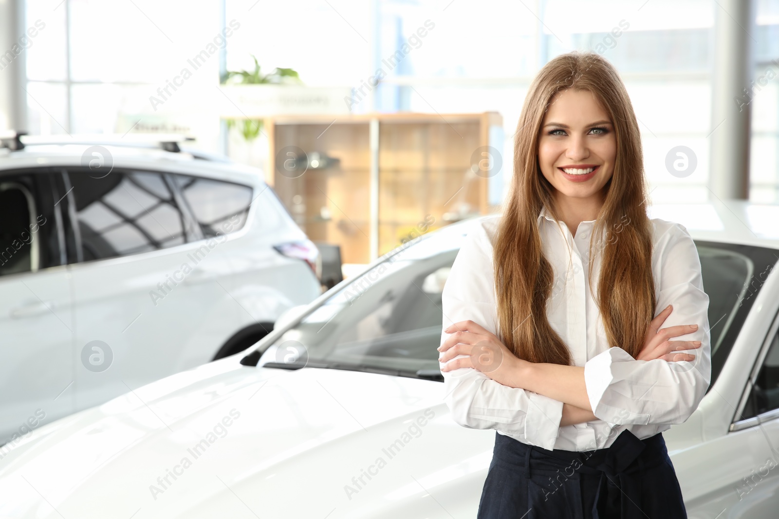 Photo of Young saleswoman standing near new car in salon