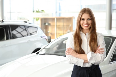 Photo of Young saleswoman standing near new car in salon