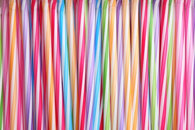 Photo of Heap of colorful plastic straws for drinks as background, closeup