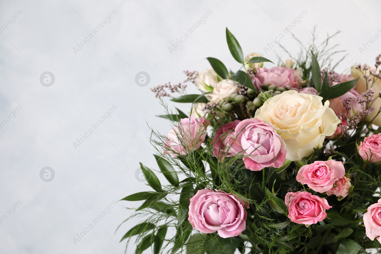 Photo of Beautiful bouquet with roses on light blue background, closeup. Space for text