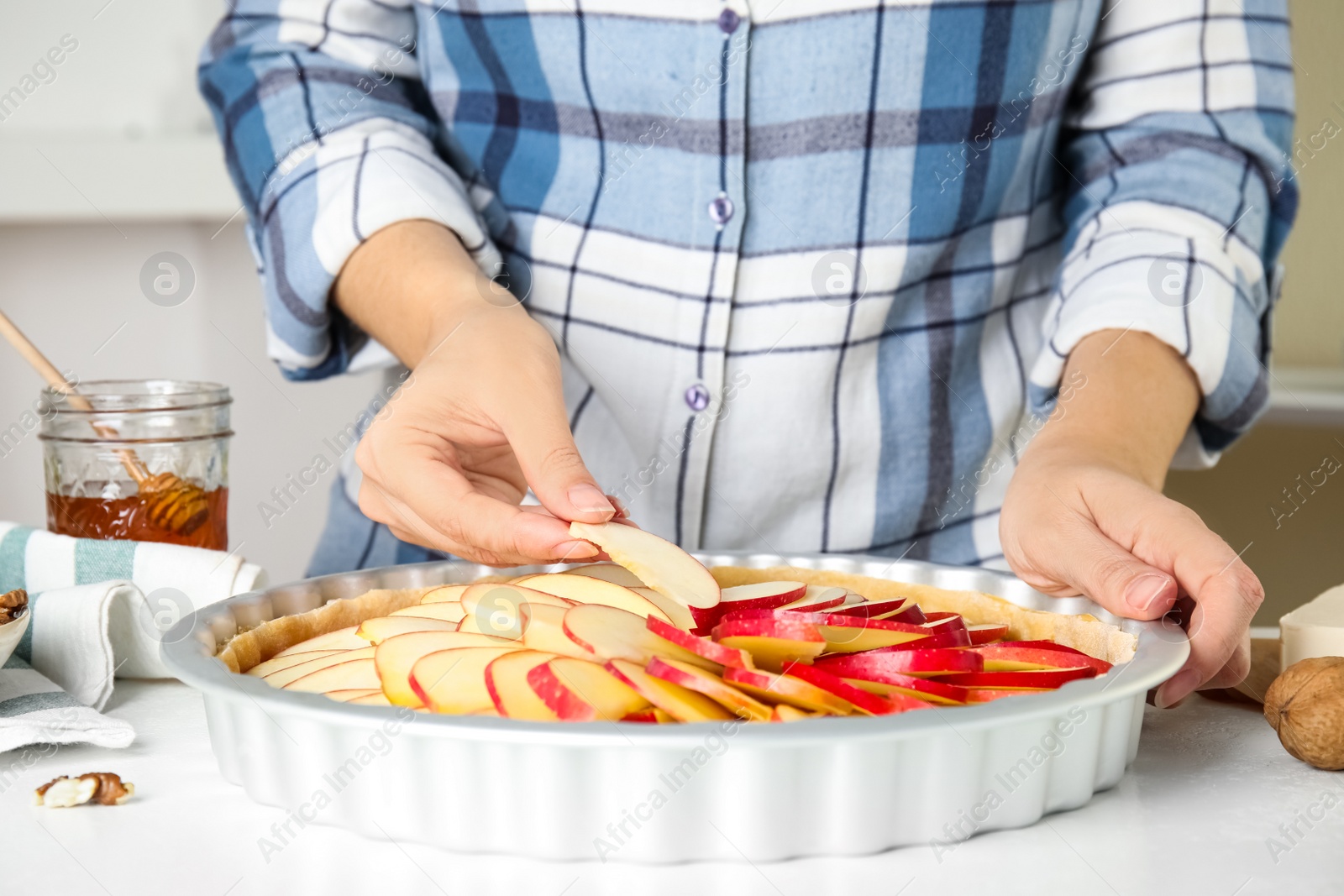 Photo of Woman putting apple slices into baking dish with dough to make traditional English pie at white table, closeup