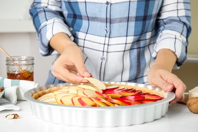 Photo of Woman putting apple slices into baking dish with dough to make traditional English pie at white table, closeup