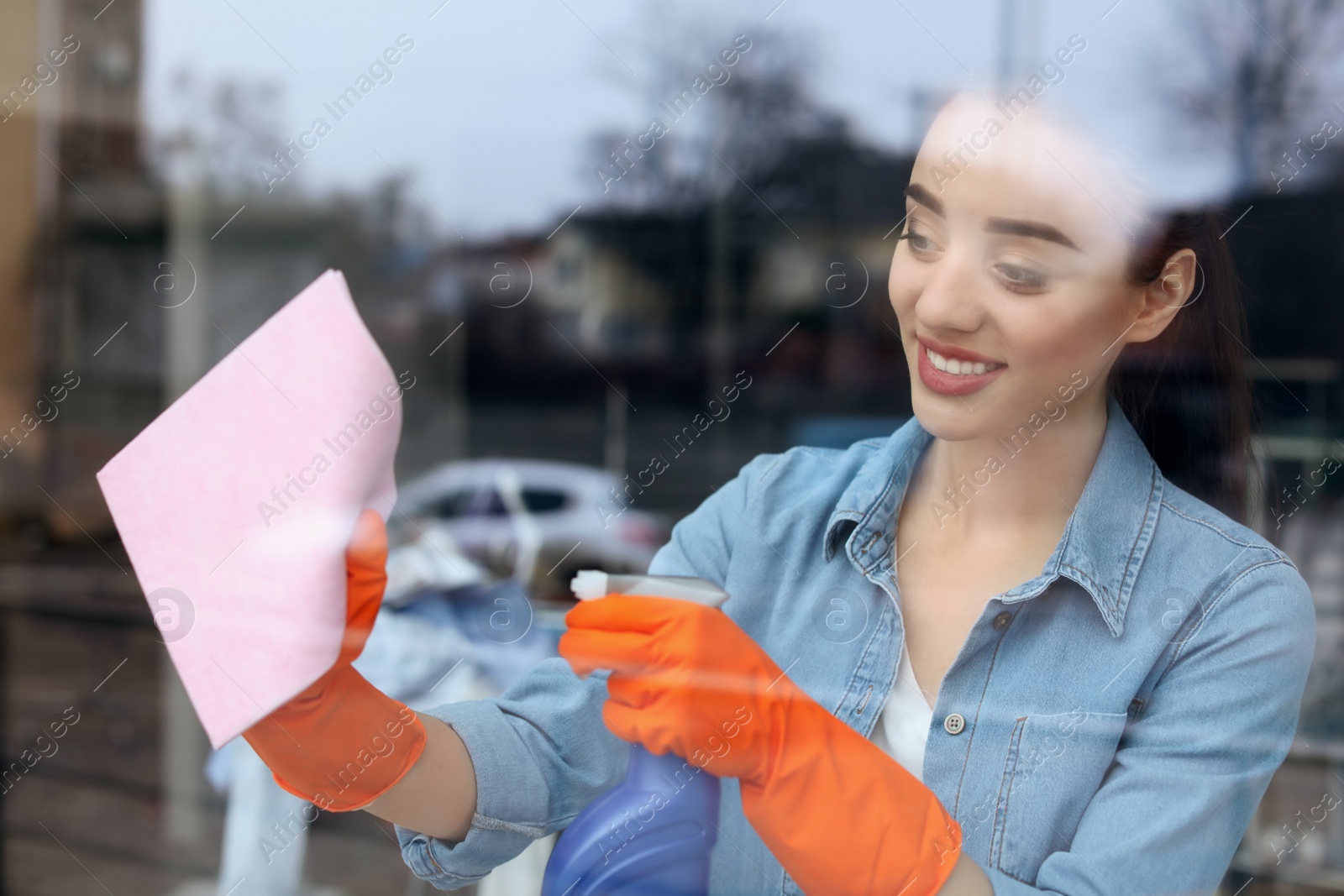 Photo of Young woman cleaning window glass at home