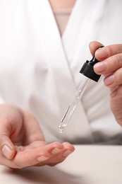 Photo of Woman applying cosmetic serum onto fingers at white table, closeup