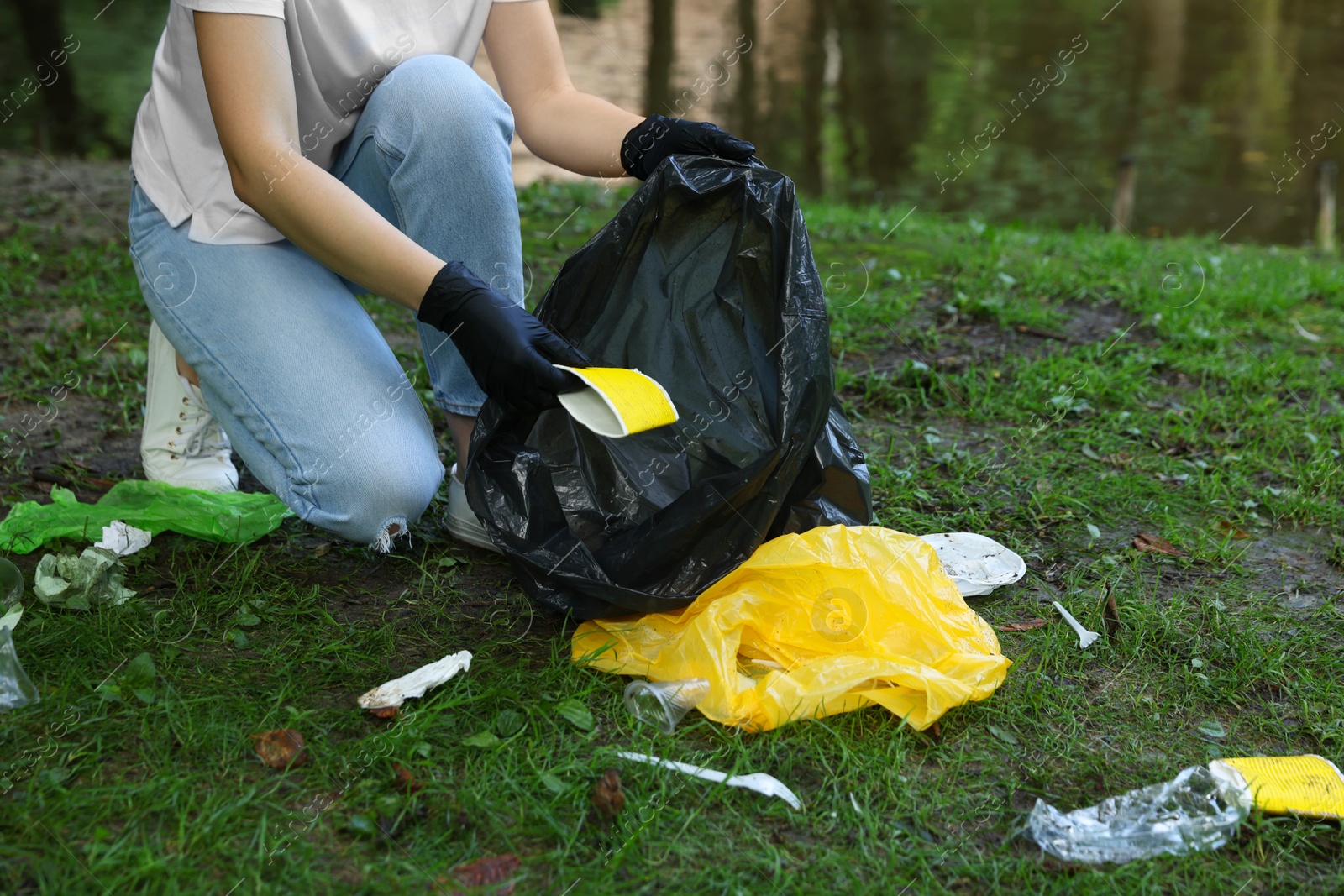 Photo of Woman with plastic bag collecting garbage in park, closeup