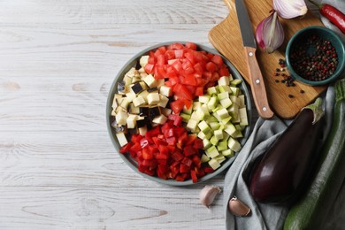 Cooking delicious ratatouille. Fresh ripe vegetables, plate and knife on white wooden table, flat lay. Space for text