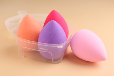 Photo of Many different makeup sponges in plastic container on beige background, closeup