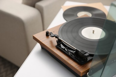 Photo of Stylish turntable with vinyl record on white chest of drawers indoors