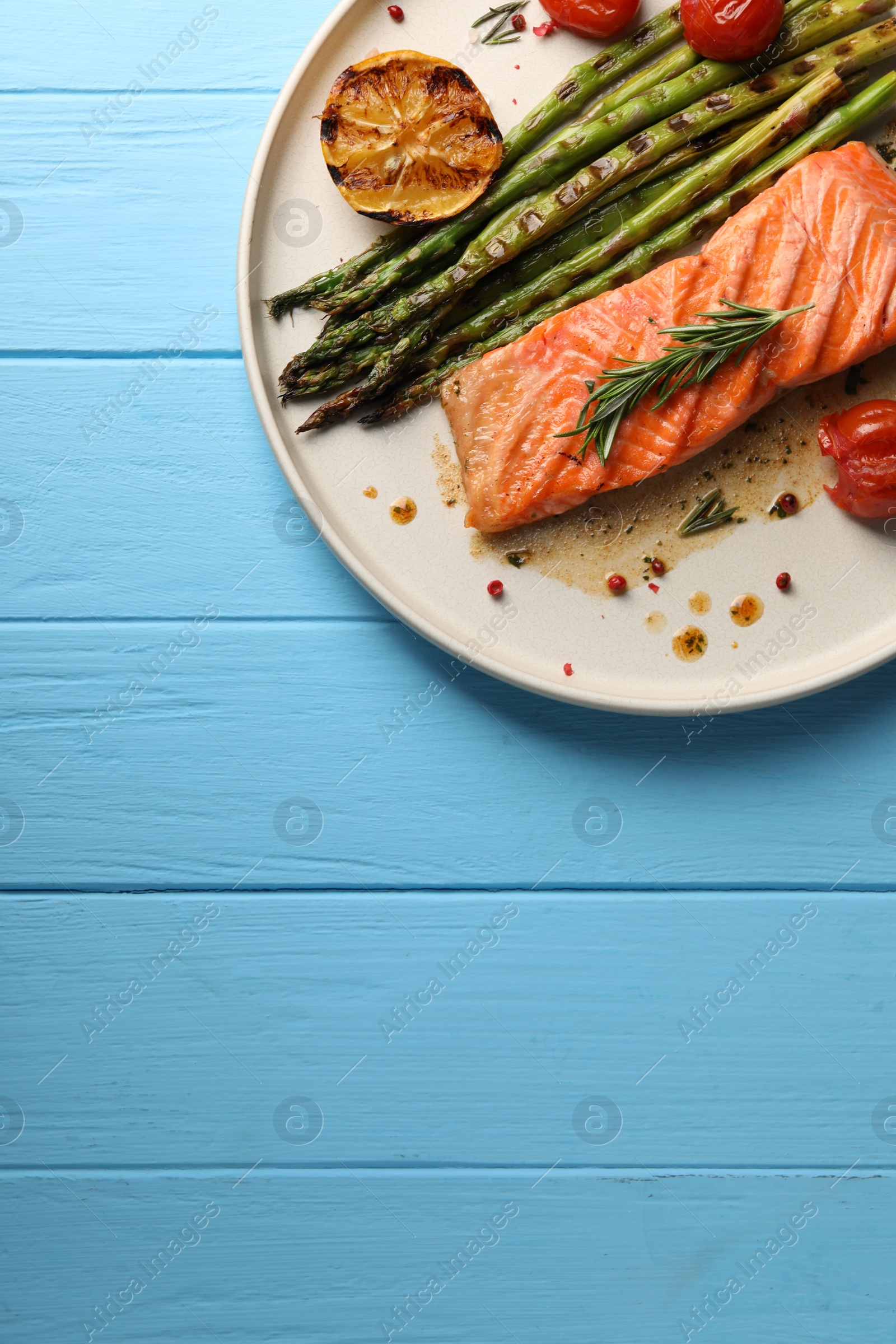 Photo of Tasty grilled salmon with tomatoes, asparagus and spices on light blue wooden table, top view. Space for text