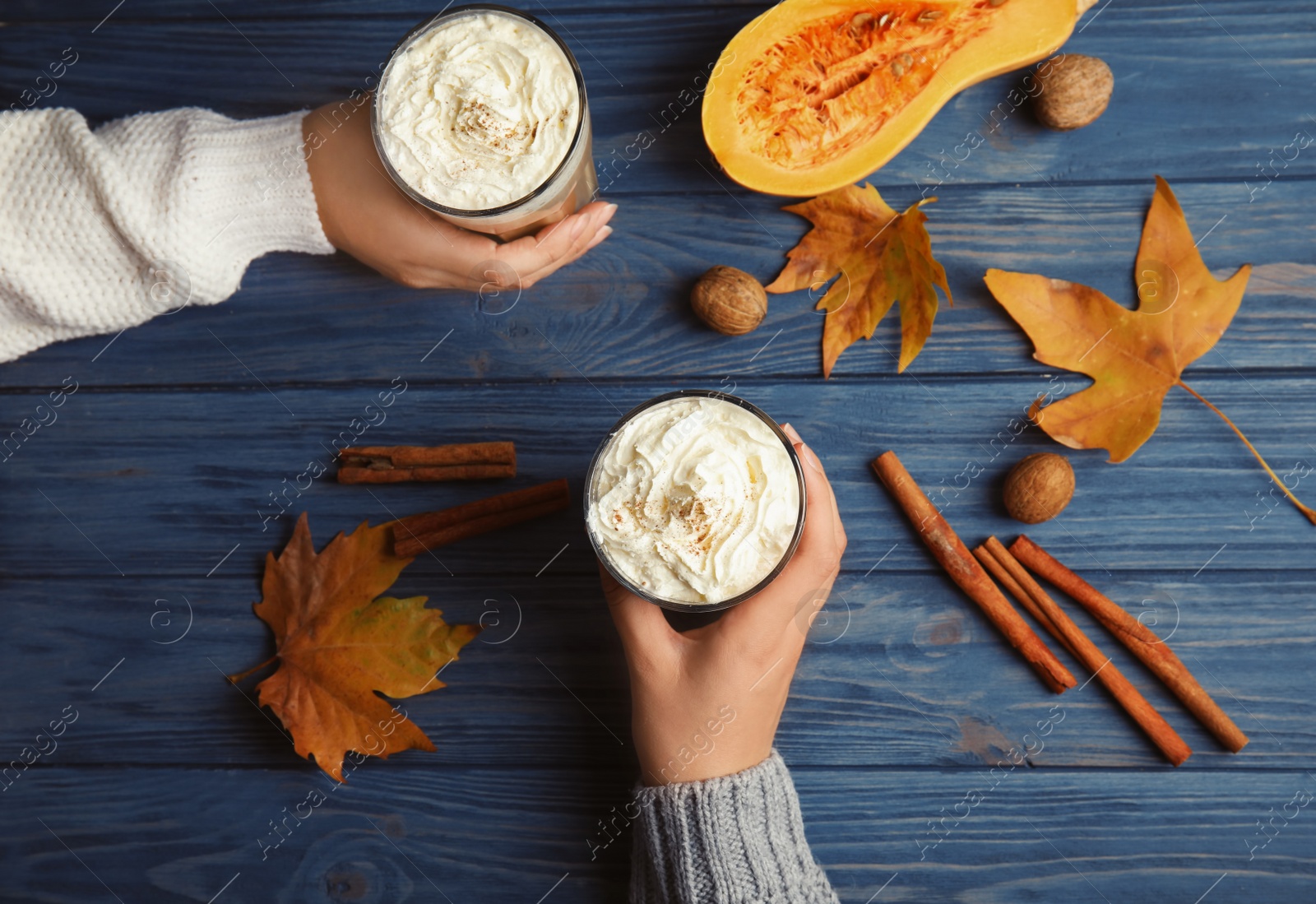 Photo of Women holding glasses with pumpkin spice latte on wooden background, top view